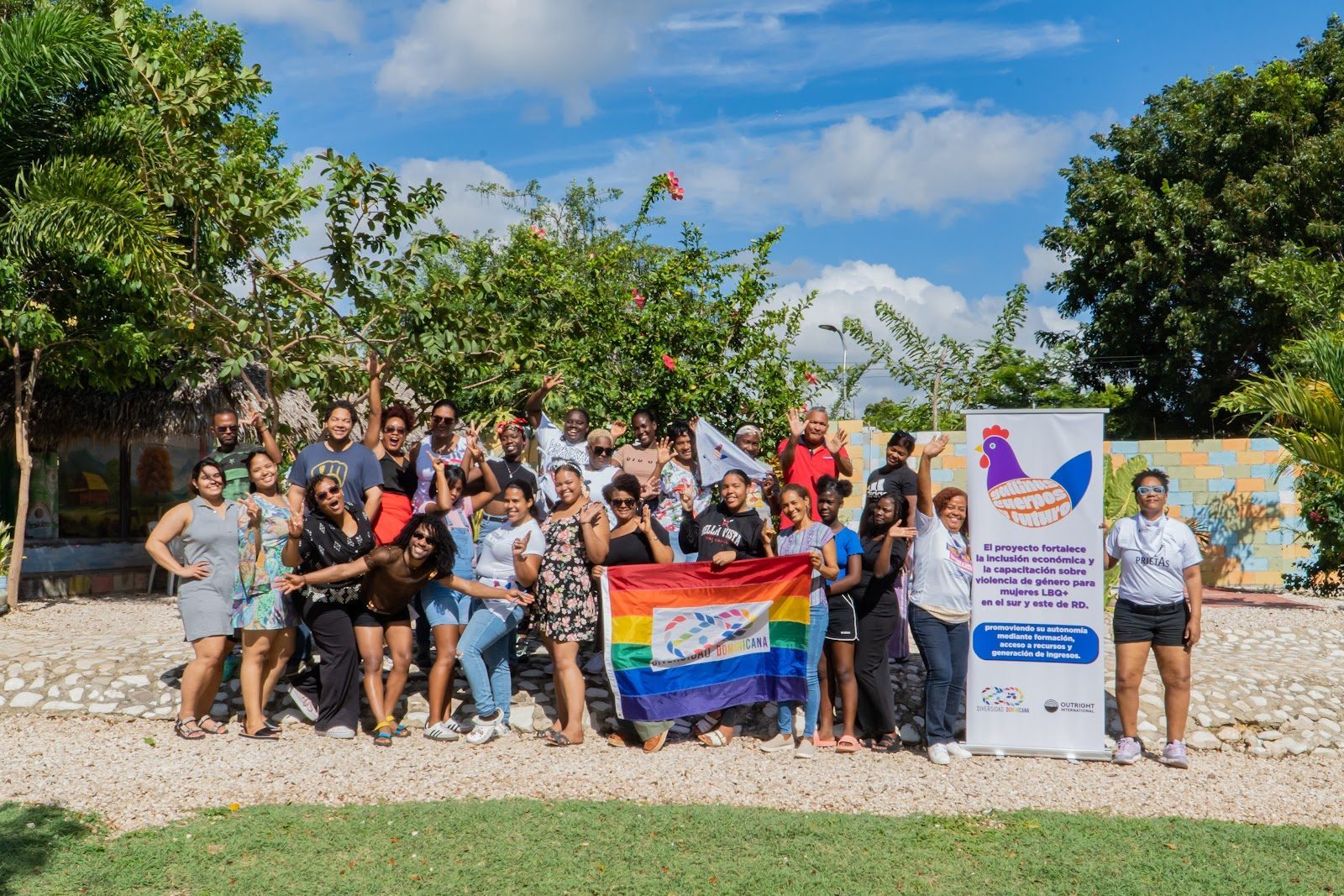 A group of women from Diversidad Dominicana pose together outdoors holding a rainbow flag