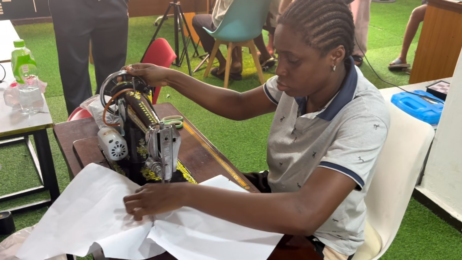 A participant sews fabric on a treadle sewing machine during a tailoring training